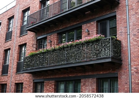 Close-up photo of modern architecture exterior with lovely balcony with small beautiful flowers blooming. Photo taken on a warm summer day.