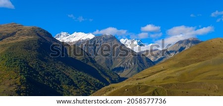 Mountain landscape with snow-capped peaks against the blue sky. Yellow autumn colors in the foreground.
