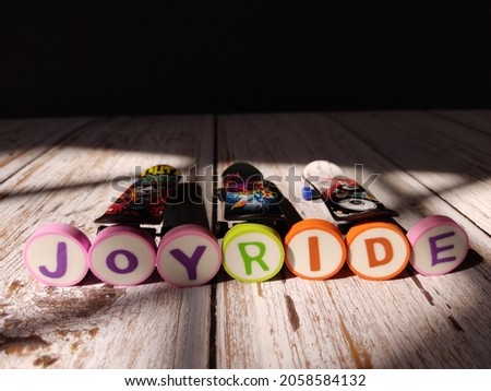 Fingerboard or small mini skateboard to play with hand fingers. The layout uses an alphabet eraser with word phrase "JOYRIDE".
