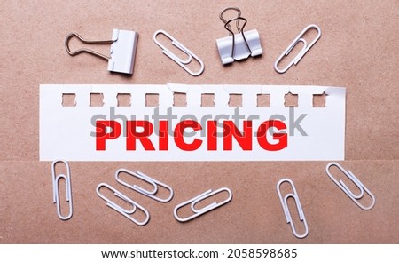 On a brown background, white paper clips and a torn strip of white paper with the text PRICING