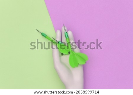 White mannequin hand holds dart needle on pink green pastel background. Top view