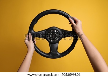 Woman holding steering wheel on yellow background, closeup Royalty-Free Stock Photo #2058599801