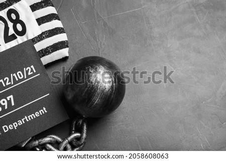 Metal ball with chain, prison uniform and mugshot letter board on grey table, flat lay. Space for text Royalty-Free Stock Photo #2058608063