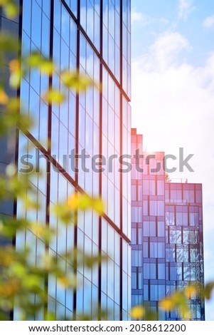 Inspiring view of the modern city. The wall of the building of glass and metal against trees. Corporate construction and ecology, view of  modern  building with blue sky and green tree. Sunlight