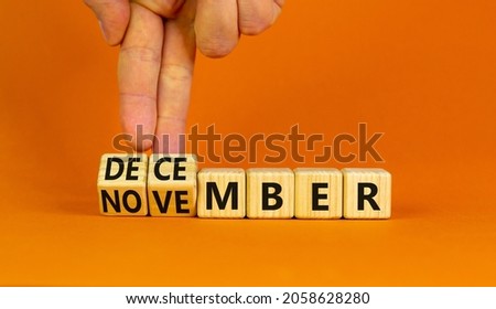 Symbol for the change from November to December, winter. Businessman turns wooden cubes and changes the word 'November' to 'December'. Beautiful orange background, copy space. Happy December concept. Royalty-Free Stock Photo #2058628280