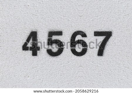 Black Number 4567 on the white wall. Spray paint. Number four thousand five hundred and sixty seven.