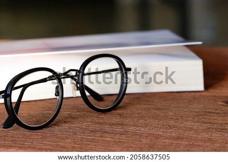 Matte black framed eyeglasses rested on a wooden floor with a blurred book background.