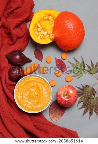Seasonal vegetables, creamy pumpkin soup and autumn leaves on grey background. Colorful picture of pumpkin soup ingredients on a table. Comfort food concept. 