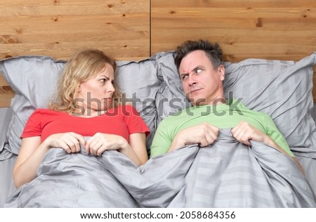 Two, a man and a woman lie on the bed and look at each other with displeasure. Relationship concept 