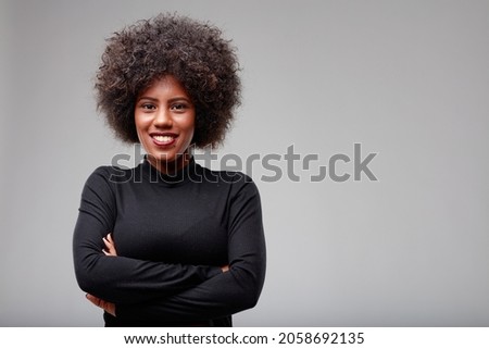 Cute trendy Young Black woman with vivacious smile standing with folded arms grinning at the camera in an upper body studio portrait with copyspace Royalty-Free Stock Photo #2058692135
