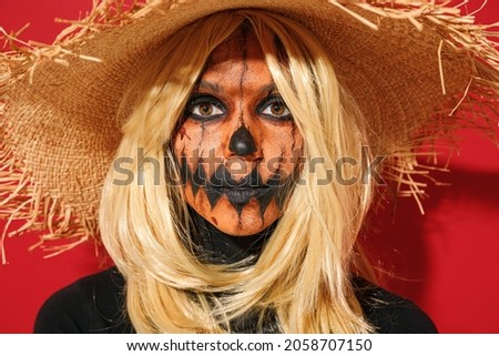 Close up young smiling woman 20s with Halloween makeup mask wearing straw hat black scarecrow costume look camera isolated on plain red background studio portrait. Celebration holiday party concept
