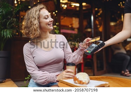 Young fun woman in casual clothes at cafe buy breakfast sit at table hold wireless modern bank payment terminal to process acquire credit card payments relax in restaurant during free time indoors. Royalty-Free Stock Photo #2058707198