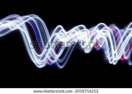 Long exposure photograph of vibrant white, red and blue colour in an abstract smoky swirl against a black background. Light painting photography