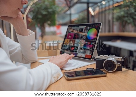 A photographer or retoucher works remotely with a laptop in a public space or coworking. A young woman in a white jacket works with images, a designer or a social media manager