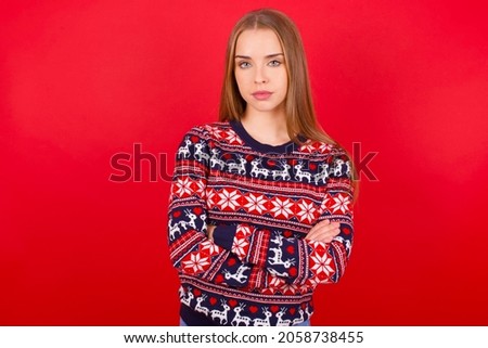 Serious pensive Young beautiful caucasian girl wearing christmas sweaters on red background feel like cool confident entrepreneur cross hands.