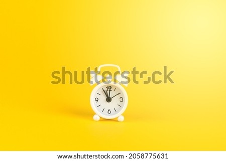 A bright studio shot of a white vintage alarm clock on a yellow background