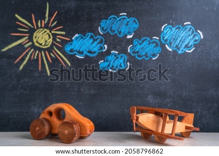 Wooden toys an airplane and a car are standing next to each other, a chalk board in the background with a picture of the sun and clouds. Selective focus