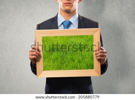 Close up of businessman holding frame with green grass
