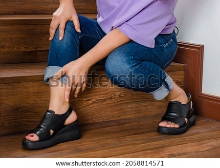 Woman loses control and cannot walk on stairs, she stops and hold her legs for support and rest with feel tingling. Concept of Guillain barre syndrome and numb legs disease or vaccine side effect. Royalty-Free Stock Photo #2058814571