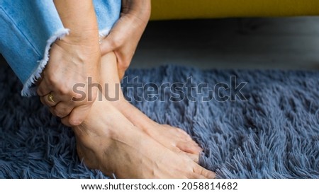 Woman sitting on sofa using hand to hold leg and feeling pain, suffer, hurt and tingling. Concept of Guillain barre syndrome and numb hands disease effect.