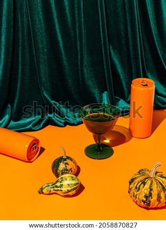 Pumpkins, green glass and orange cans against plush velvet curtain background. Creative Halloween and Thanksgiving table concept. Contemporary fall still life idea.