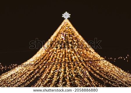 Golden Christmas tree with bokeh lights background. Xmas abstract glowing decorations outdoors. Glitter lights backdrop. Winter season.