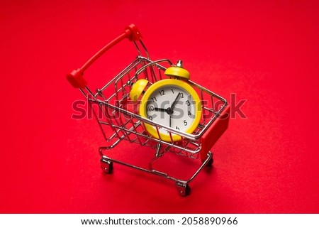 Shopping time. Yellow alarm clock in shopping basket on a red background. Copy space. 
