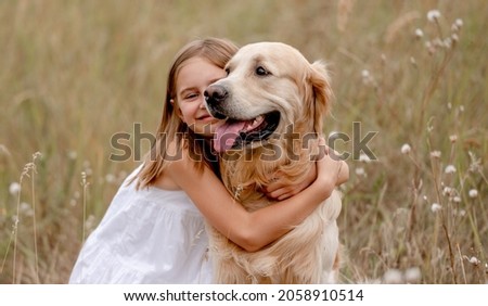 Little girl hugging golden retriever dog in the field in summer day together. Cute child with doggy pet portrait at nature Royalty-Free Stock Photo #2058910514
