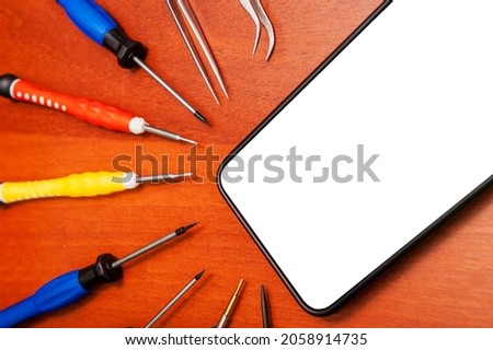A mobile phone with an empty screen is lying on a table with repair tools, close-up, white screen.