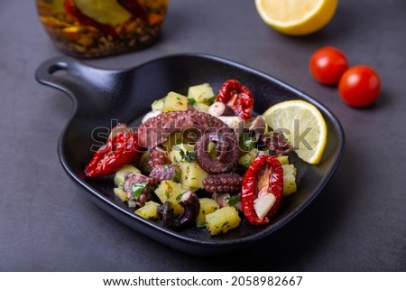 Warm salad with octopus, potatoes, sun-dried tomatoes, garlic and lemon in a black small pan. Close-up, black background.