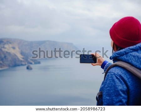 A woman take a photo of the sea on smartphone, female travels along the coast in the cold season. Outdoor. POV. Close up
