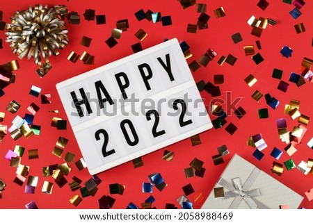  lightbox with words happy 2022, gift box and holiday confetti on red background. top view new year celebration. party background.