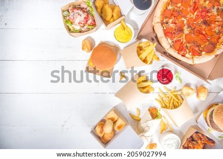 Delivery fastfood ordering food online concept. Large set of assorted take out foods pizza, french fries, fried chicken nuggets, burgers, salads, chicken wings, various sides, white table background  Royalty-Free Stock Photo #2059027994