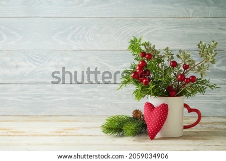 Christmas pine tree branches in coffee cup and heart shape ornament on wooden table background