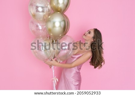  smiling cute adult girl with golden air balloons laughing on pink background. Happy beautiful Young woman on birthday new year holiday party having fun and celebrating. 8th March. Valentine's day 