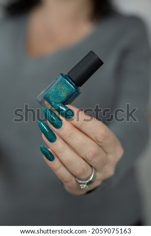 Woman hand with long nails and turquoise blue green manicure with bottles of nail polish