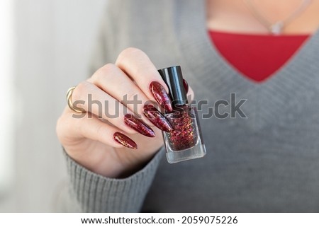 Woman's hands with long nails and a bottle of bright red nail polish