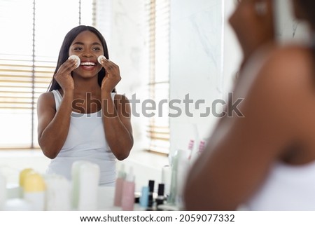Daily Skincare. Beautiful Smiling Black Woman Cleansing Skin With Cotton Pads And Looking At Mirror, Young African American Lady Removing Make Up In Bathroom At Home, Selective Focus On Reflection Royalty-Free Stock Photo #2059077332