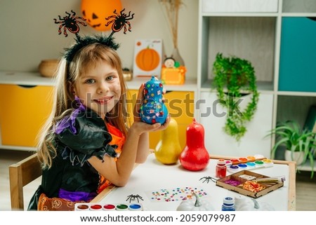 Little girl in whitch costume holding decorated blue painted pumpkins with shine stickers. Idea for Halloween DIY art class for children. Selected focus.