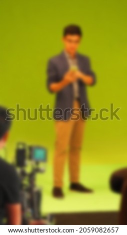 Blurry images of making TV commercial movie video in big green screen background. Film crew team working with actor. Recording by professional digital camera and lighting set. film behind the scenes