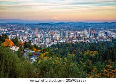 Scenic overlook from Pittock Mansion in Fall of Portland downtown with Mt Hood drenched in the orange light of the setting sun and waxing gibbous moon on the side.