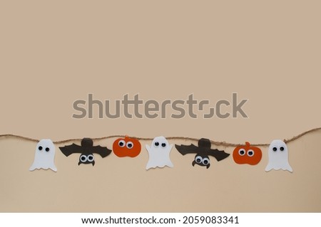 homemade garland on a jute rope made of pumpkins, bats and ghosts with eyes on a beige background with a place for text