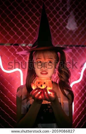 Charming witch holding halloween  pumpkin candle cup in red light on dark background