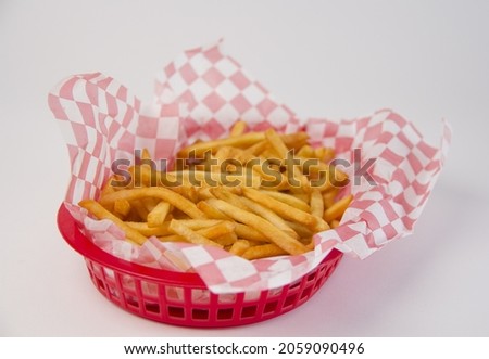 A closeup of french fries in a plastic basket with a checkered pattern on a white background