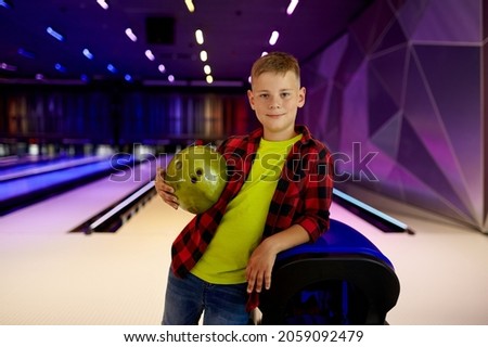 Boy with ball poses at the lane in bowling alley
