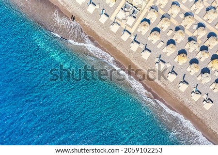 Top view aerial drone photo of black Perissa beach with beautiful turquoise water, sea waves and straw umbrellas. Vacation travel background. Aegean sea, Santorini Island, Greece.