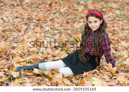 smiling teen girl in school uniform sitting in autumn leaves outdoor, september