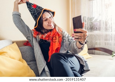 Halloween. Woman in witch hat taking selfie using smartphone. Celebrating holidays at home during coronavirus lockdown