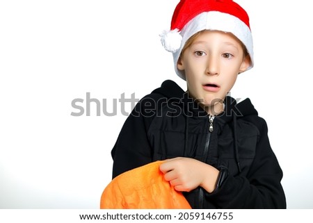 a boy in a red Santa hat put his hand into a yellow bag and opened his mouth in surprise