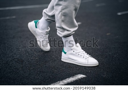 Women's legs in sweatpants, white socks and white sneakers with green elements against the background of the track with markings in the stadium. Royalty-Free Stock Photo #2059149038